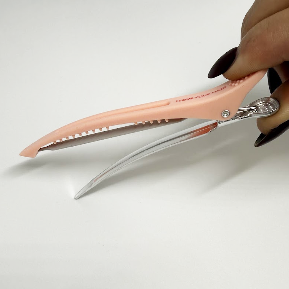 Pink sectioning clip held by a hand on a white background